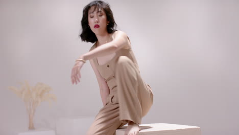 after pause asian woman entering studio by block sliding onto beige cube showing beige outfit