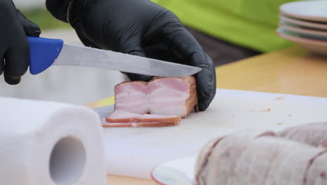 knife slicing pork belly meat on bright cutting board in clean food prep area with kitchen tools