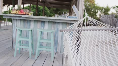 empty hammock swinging and stools by the counter at beach bar, in slow motion