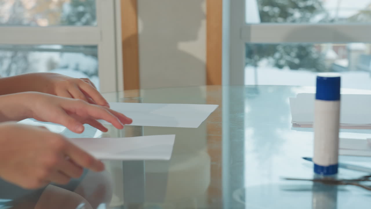 Hand view of three persons, one giving two others white paper, white marker, and scissors on table, focus on hands exchanging materials in cozy, bright home setting