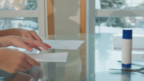 hand view of three persons, one giving two others white paper, white marker, and scissors on table, focus on hands exchanging materials in cozy, bright home setting