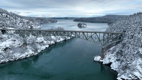 wide aerial view pulling away from deception pass with fresh snow on the ground