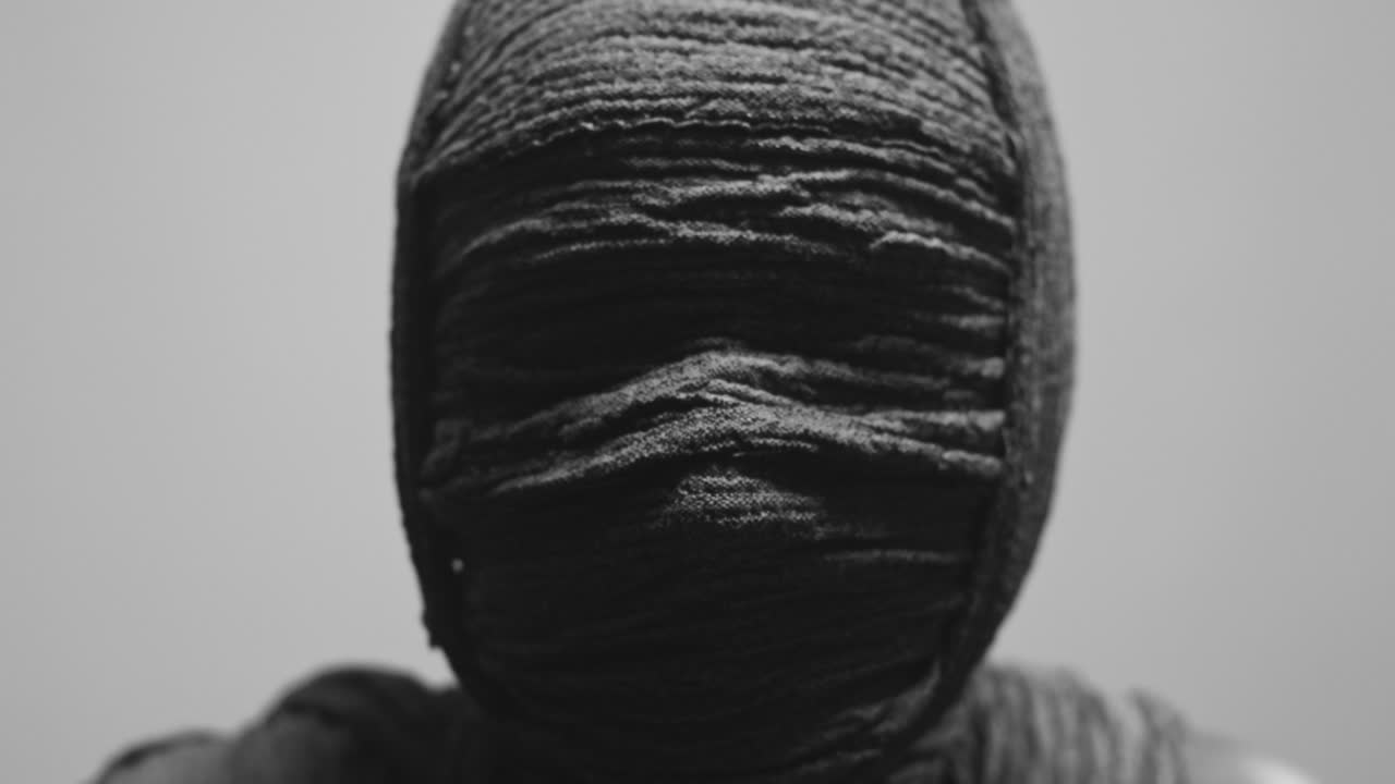 A mummy of a woman on a white backdrop slowly rises her head