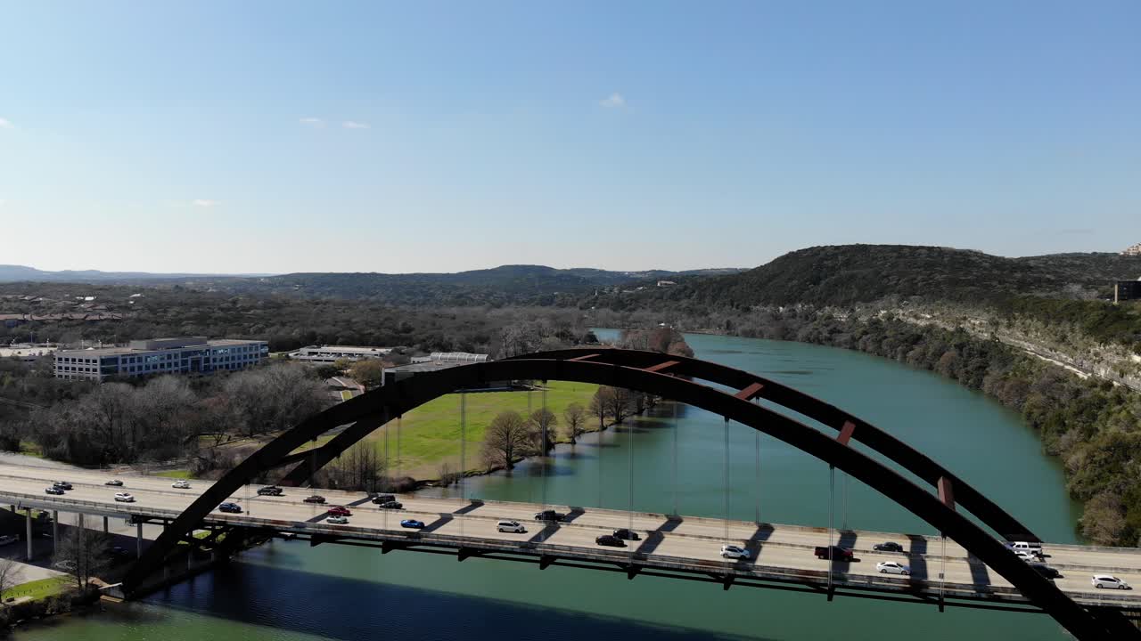 Aerial Austin Pennybacker Bridge - panning right to get the bridge - river in full view. Lots of traffic on the deck, backed up to the other side of the bridge before traffic begins to move again