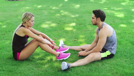 Pareja-Deportiva-Descansando-Sobre-El-Césped-Después-De-Hacer-Ejercicio-Al-Aire-Libre.-Joven-Y-Mujer