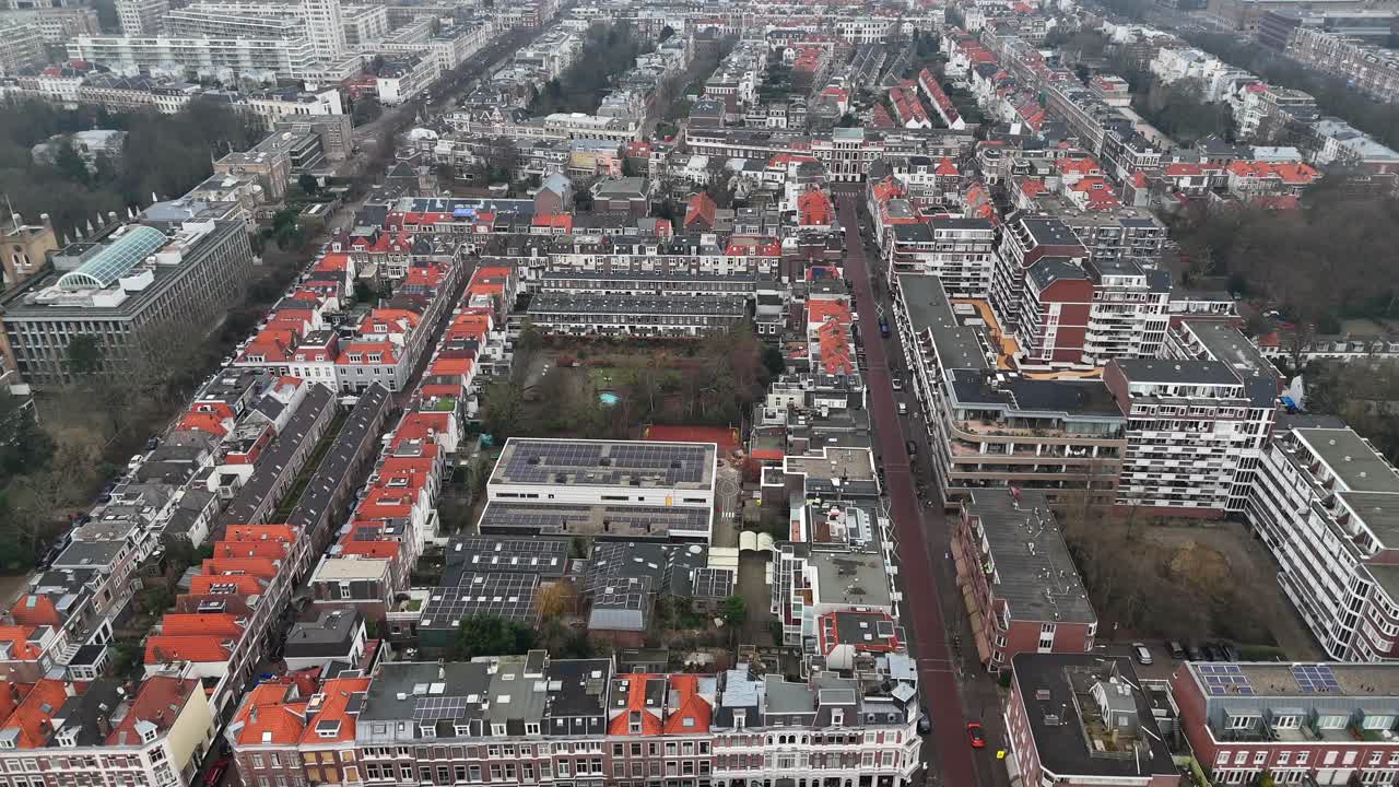 Dense row of homes and park with playground in center. Solar panels on roof of houses in dutch neighborhood. Cold winter day in The Hague town, Netherlands. Aerial flyover shot.
