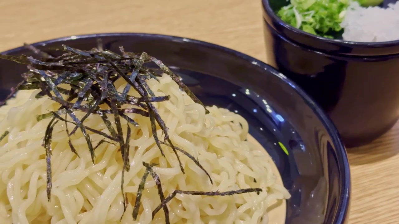 Primo piano di noodles giapponesi freddi serviti con condimenti freschi e salsa per intingere, creando un pasto rinfrescante con sapori puliti e una presentazione elegante