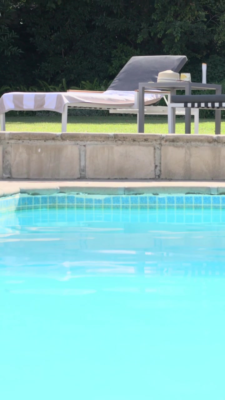 Vertikal video: Kamera vipper og afslører blå pool derhjemme, viser liggestole og stribet håndklæde.