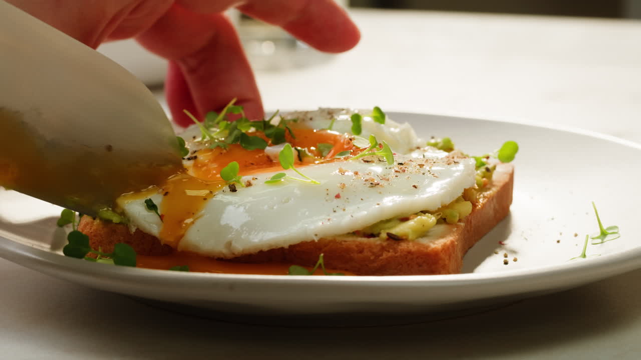Hand Carefully Cutting Sunny-Side Up Egg on Avocado Toast