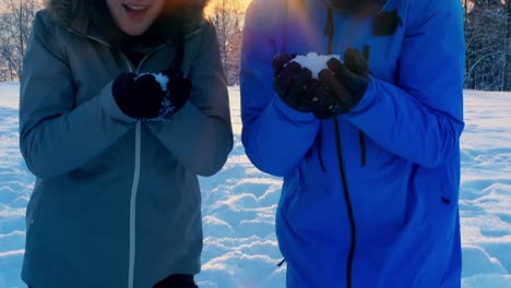 couple blowing snow in snowy forest