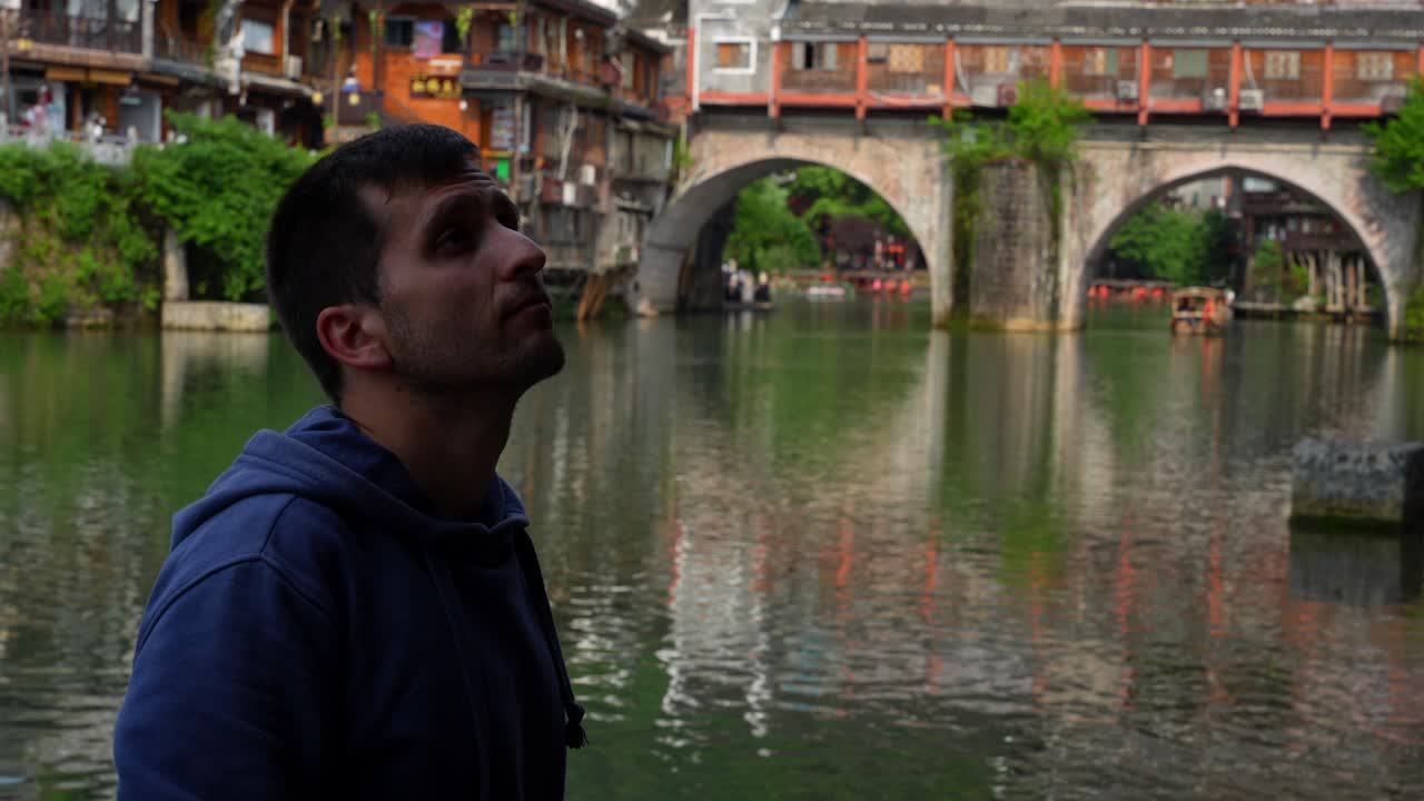 Tourist man watching the scenery near Rainbow Bridge in Tuojiang River. Fenghuang, China