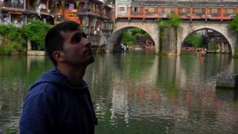 tourist man watching the scenery near rainbow bridge in tuojiang river. fenghuang, china