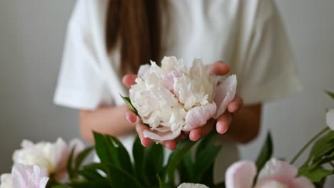 crop girl standing and holding peony flower of green leaves plant in hands