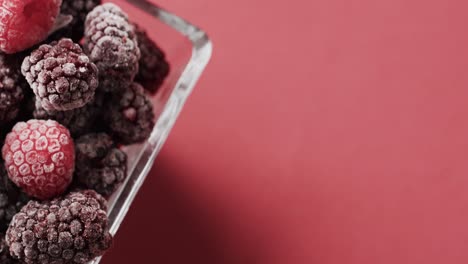 Micro-video-of-close-up-of-raspberries-in-bowl-with-copy-space-on-red-background