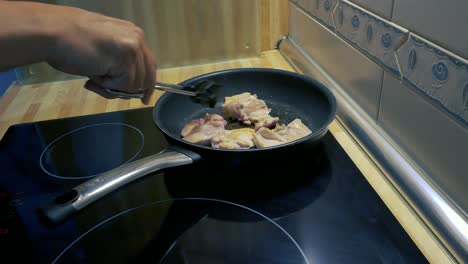 los brazos de un hombre girando alrededor de un muslo de pollo filetes en una sartén