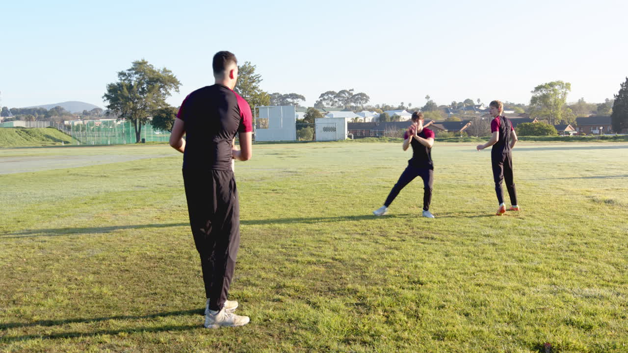 Three multiracial male cricket players practicing cricket on pitch
