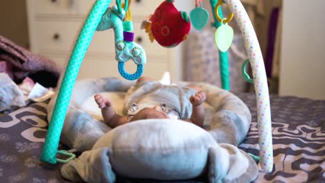 Adorable-Newborn-Baby-in-Cradle-Staring-at-Colorful-Toys-Above-Her-and-Moving-Small-Legs-and-Hands