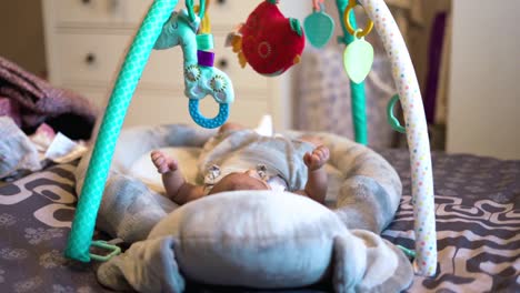 adorable newborn baby in cradle staring at colorful toys above her and moving small legs and hands