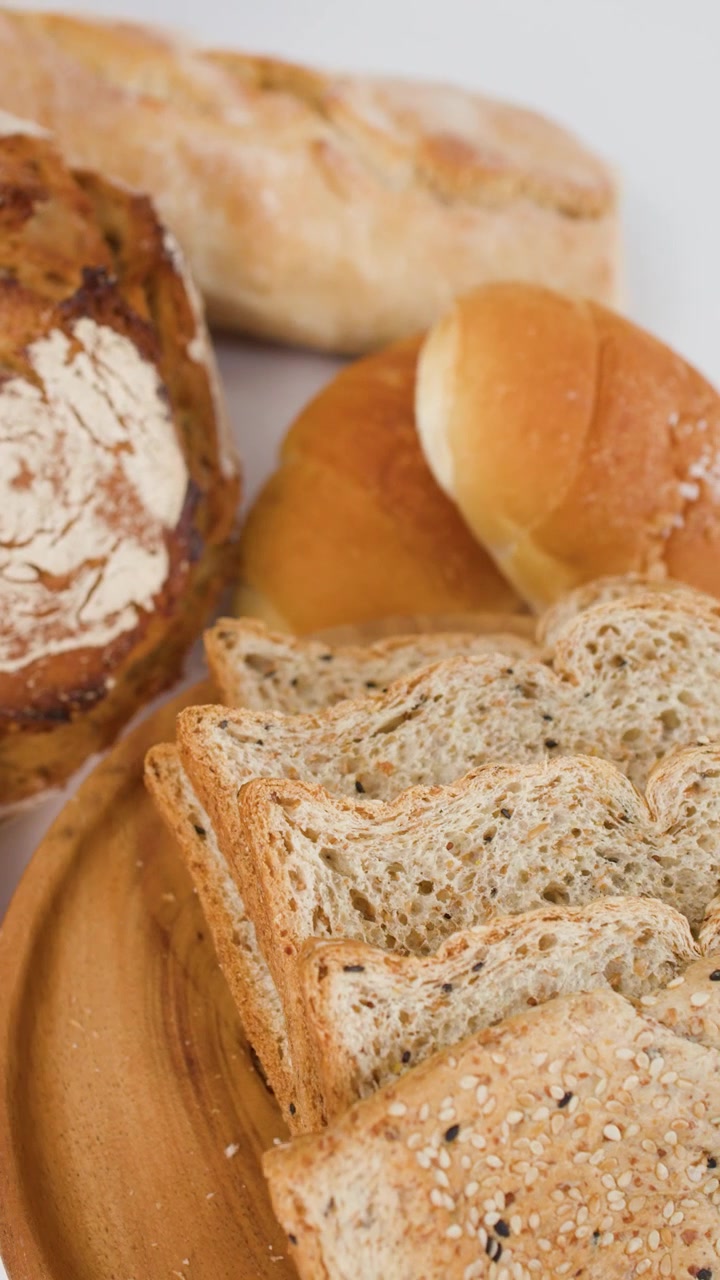 Vista ravvicinata e rotante di pane a lievitazione naturale, baguette e toast integrale con semi su un vassoio di legno.