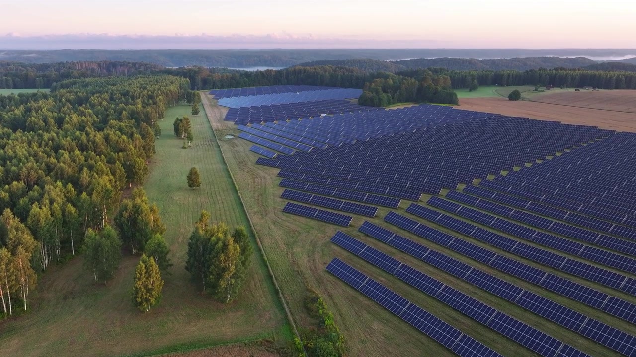 Luftfoto fra drone af en stor solcellepark nær Sigulda, Letland, omgivet af skove, landbrugsmarker og et naturskønt landområde.