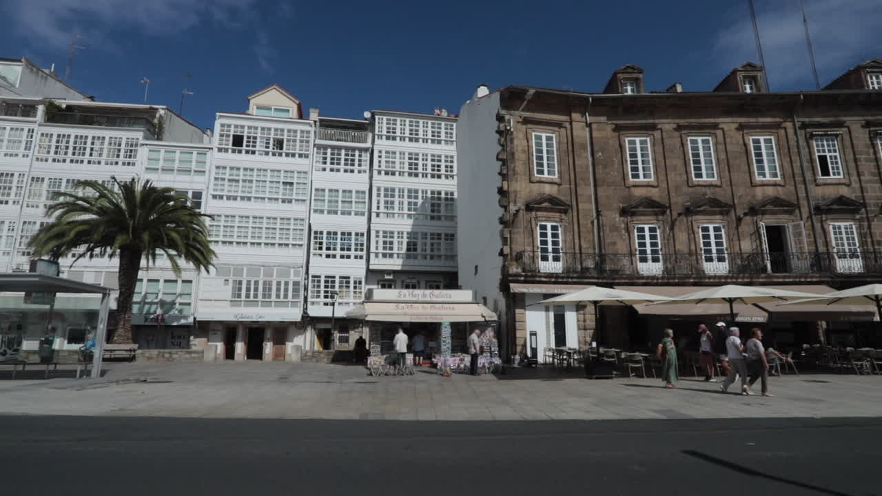 Sunny day street view of people walking past historic buildings and outdoor cafes
