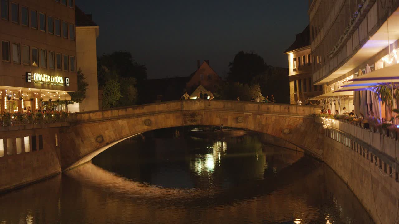 Stone bridge, riverside restaurants, and reflections at night with warm ambient lighting, static camera