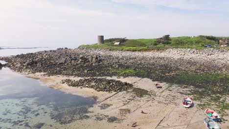 Imágenes-Amplias-De-Drones-Siguiendo-La-Costa,-Playa-Durante-La-Marea-Baja-Sobre-Rocas-Con-Un-Mar-Con-Acabado-De-Espejo-Y-Luz-Mística-Y-Mar-Cristalino-En-Guernsey