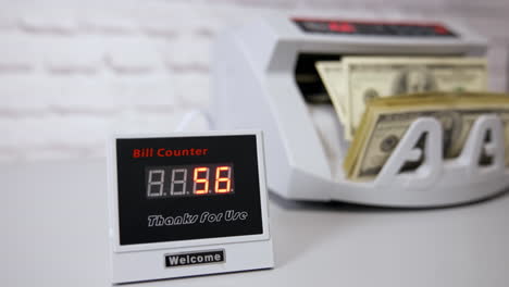 us dollar bills. woman putting money into counting machine at table indoors, close up.
