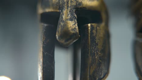 a close-up macro shot of a spartan design, two different ancient warrior metal bronze helmets, textured shapes, studio lighting, full hd cinematic video, hyper slow motion 120 fps, pan right