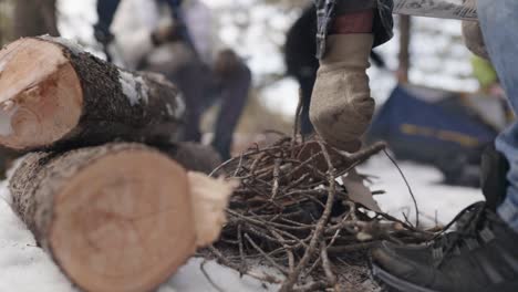Man starting small fire with cardboard and twigs on snowy ground