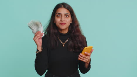 Mujer-India-Usa-Un-Teléfono-Inteligente-Regocijándose-Por-Ganar,-Recibiendo-Dinero-En-Efectivo-En-Dólares,-Suerte-En-El-Premio-Mayor-De-Lotería-De-éxito