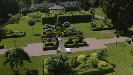 Newlyweds,-caucasian-groom-with-bride-walking,-embracing,-hugs-making-a-kiss-in-park,-wedding-couple