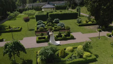 newlyweds, caucasian groom with bride walking, embracing, hugs making a kiss in park, wedding couple