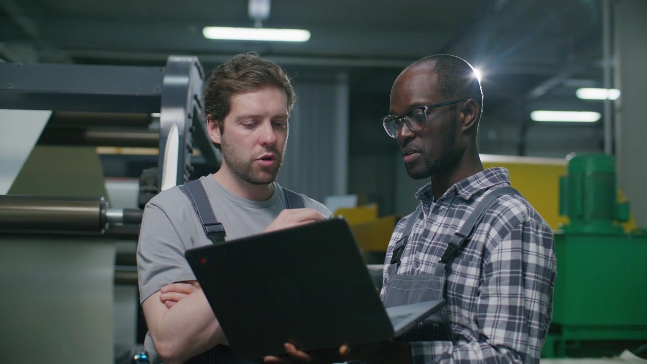Diverse Industrial Print Shop Operators Troubleshooting Machinery with Laptop