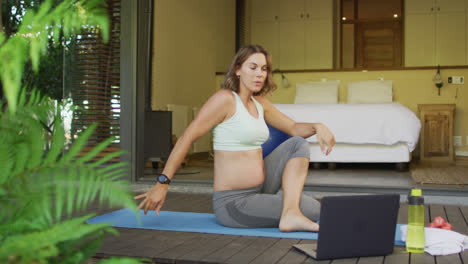 mujer caucásica embarazada practicando yoga en casa con lecciones en línea