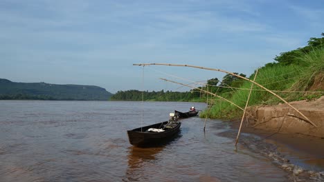 long boats moored at the edge of the mekong river with gentle waves lapping the shore