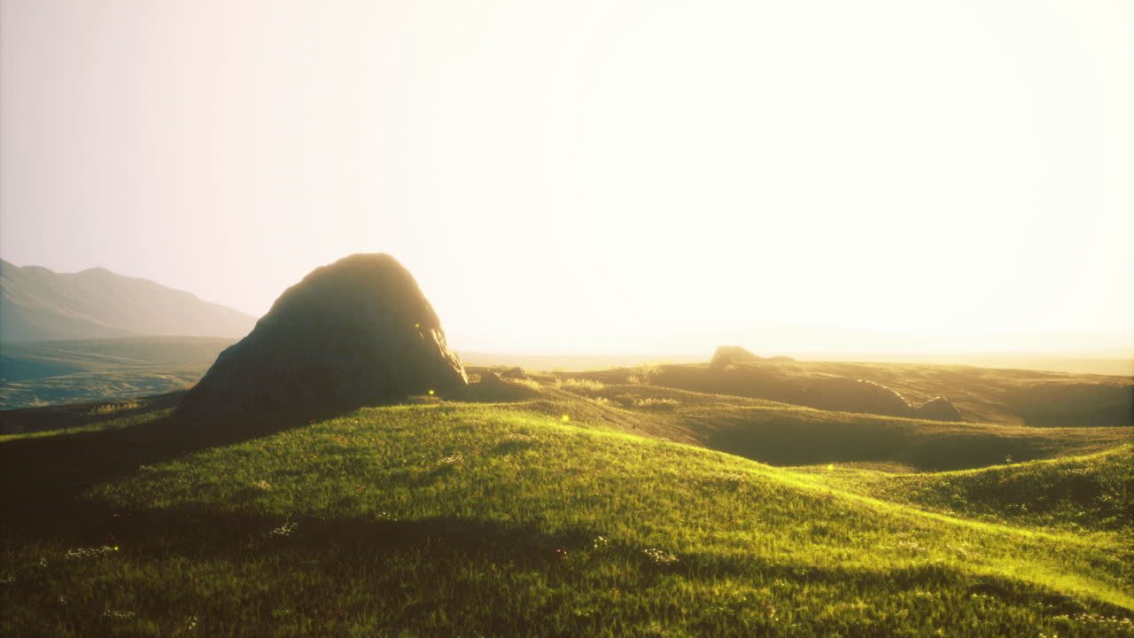 Sunlight glows warmly over serene grassy hills and rocky formations