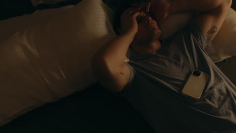 hombre agotado saltando a la cama con el teléfono en el pecho, por la noche