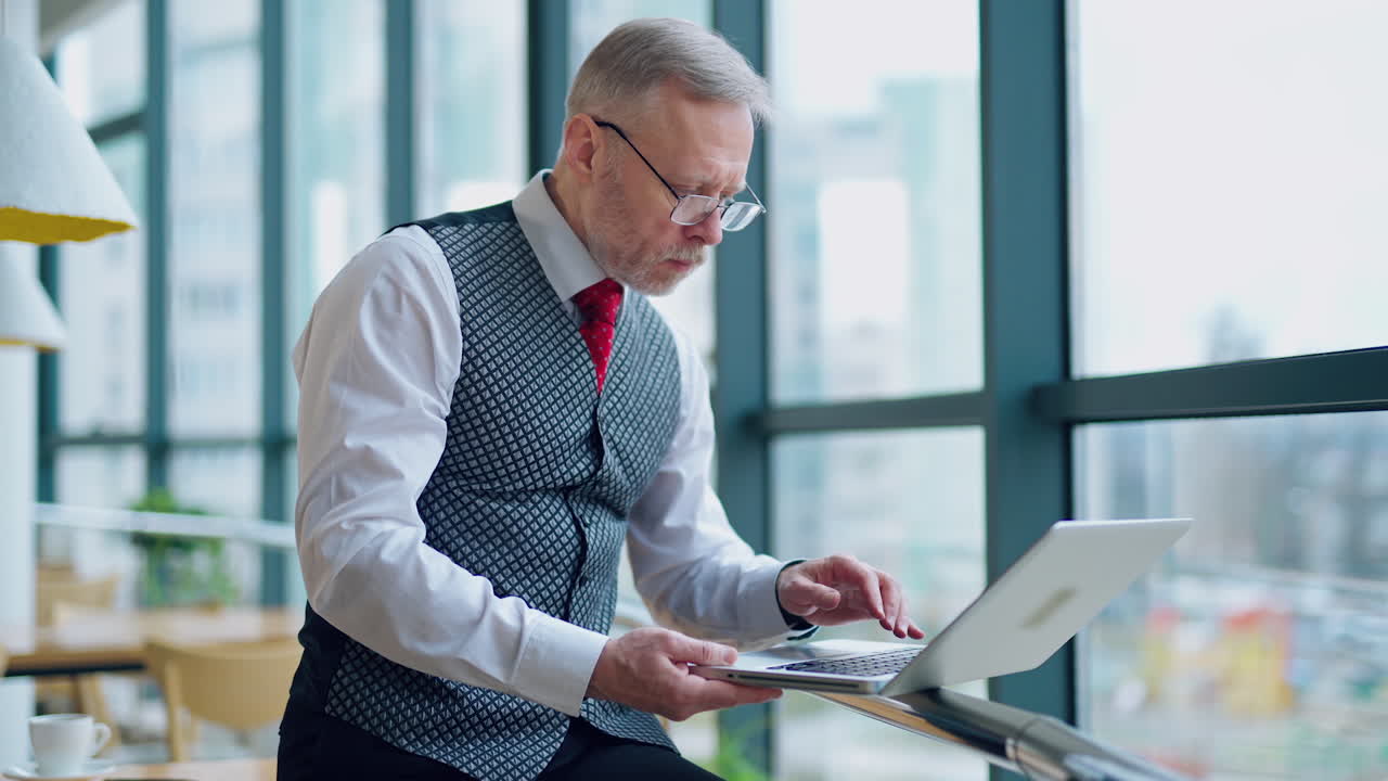 Thoughtful businessman working on computer in front of the window with city view. Video of working process in big company.