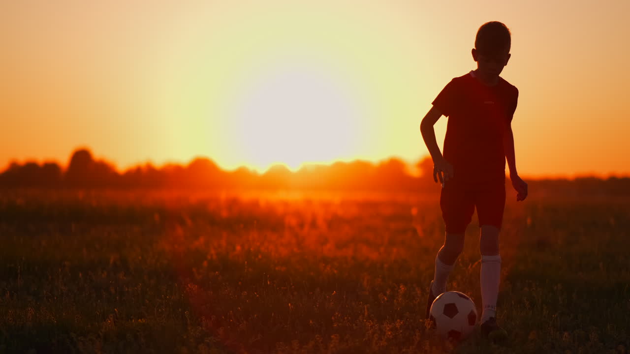 niño jugador de fútbol al atardecer corre con una pelota de fútbol en el campo de entrenamiento regateando desde el amanecer hasta el anochecer. camino al éxito. el concepto de lograr la meta de un atleta exitoso