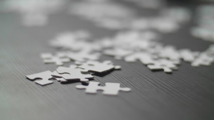 Primo piano di pezzi di puzzle bianchi disposti casualmente su un tavolo scuro. Ripreso in 4K con profondità di campo ridotta. Movimento fluido del dolly della telecamera lungo il tavolo
