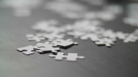 close up of white puzzle pieces laying randomly on a dark table. shot in 4k with shallow depth of field. smooth camera dolly movement along the table