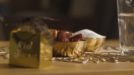 bowl of dates with glass of water and gift boxes on table in muslim home celebrating eid 4