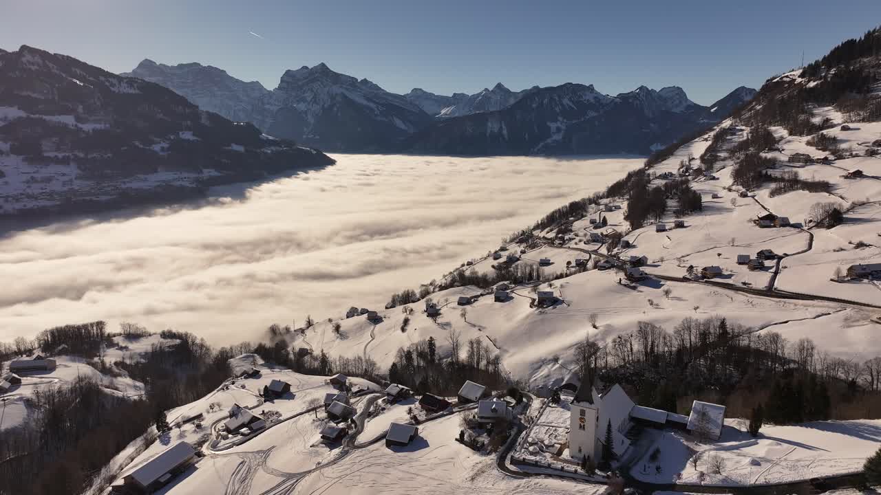 Drone flight over Amden, a picturesque village in the Swiss Alps, fully covered in snow on a typical winter day.