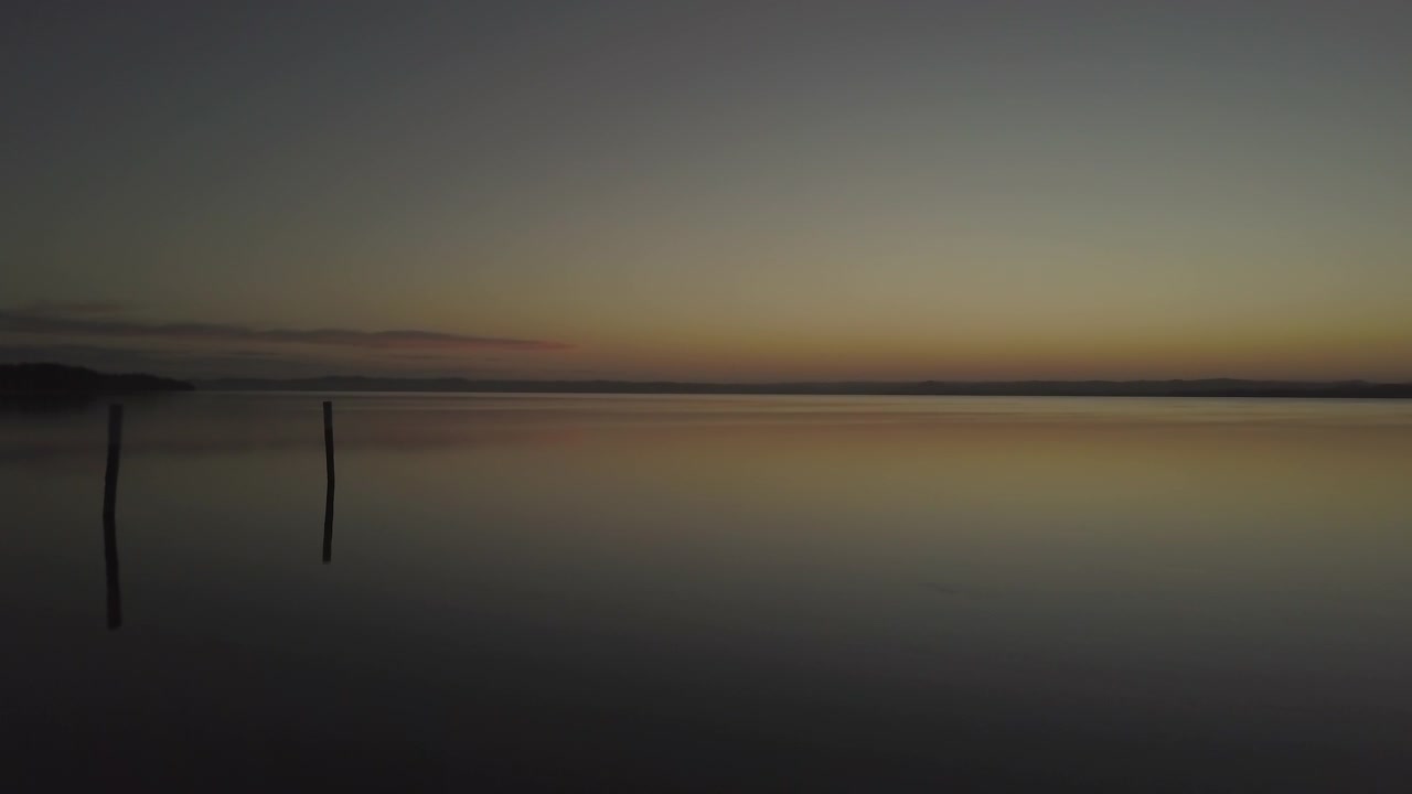 Smooth forward aerial motion over calm mirror-like body of water during twilight hours.