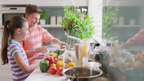 hermanos caucásicos felices desempaquetando bolsas con verduras