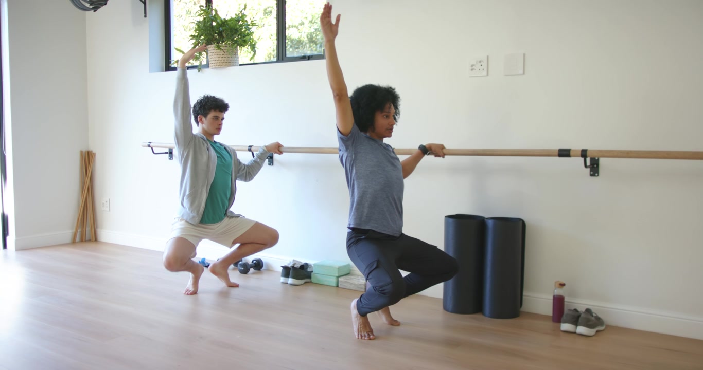 Compañeros de entrenamiento masculinos haciendo barre en un gimnasio en casa, el líder de adelante iniciando sentadillas sincronizadas para el equilibrio.