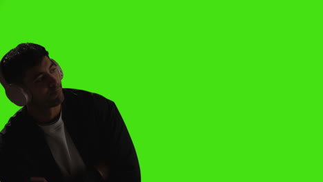 young man wearing wireless headphones and streaming music against green screen with low key lighting