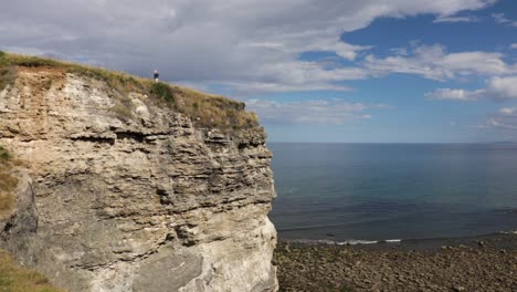 wide angle shot of lady standing on edge of cliff in summer sun, england