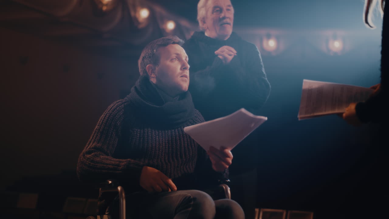 Elderly Director Giving Instructions to Actors during Rehearsal Senior Stage Director Giving Instructions to Man on Wheelchair then Watching Actors Acting out Quarrel Scene during Rehearsal in Theater